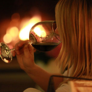 Frau mit Rotwein vor Kamin