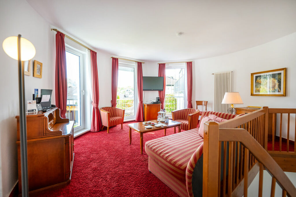 Wohnbereich der Turm Suite im Hotel Kessler-Meyer mit rotem Teppich, Sitzgruppe und großen Fenstern