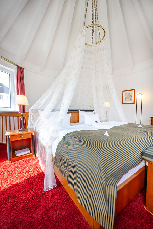 Turm Suite im Hotel Kessler-Meyer mit Himmelbett, rotem Teppich und hellem Schlafzimmer unter hoher Turmdecke
