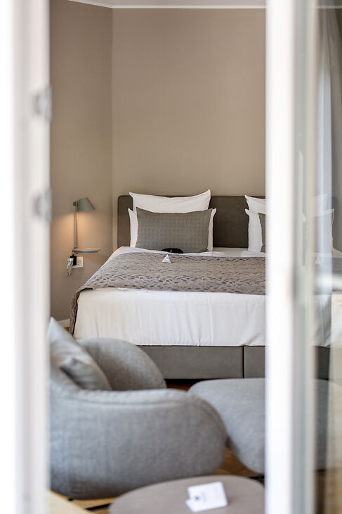 Kabinett-Zimmer im Hotel Kessler-Meyer mit Doppelbett, grauem Sessel und gemütlichem Wohnbereich