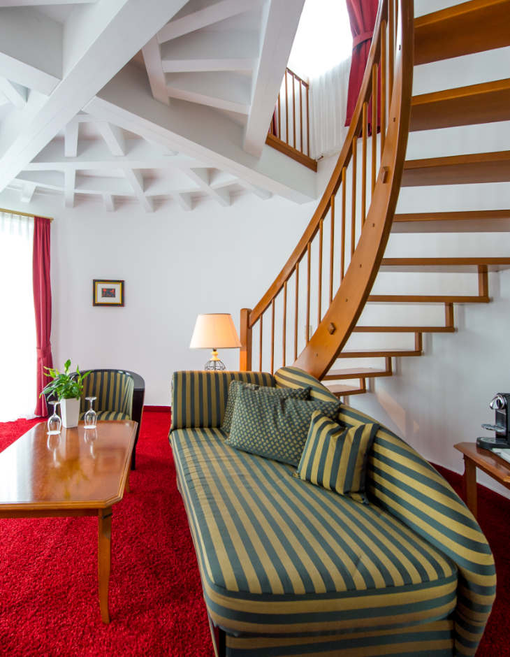 Blick auf das Sofa, die geschwungene Treppe und die stilvolle Zimmerdecke der Turmsuite