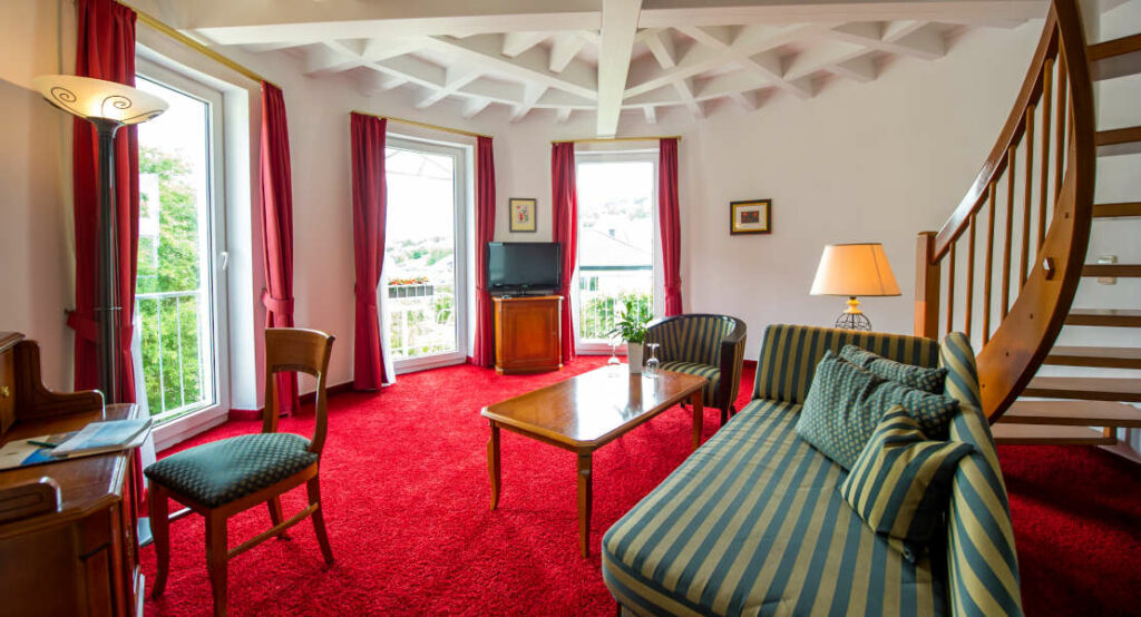 Blick auf das Sofa, die stilvolle Zimmerdecke und die drei bodentiefen Fenster in der Turmsuite