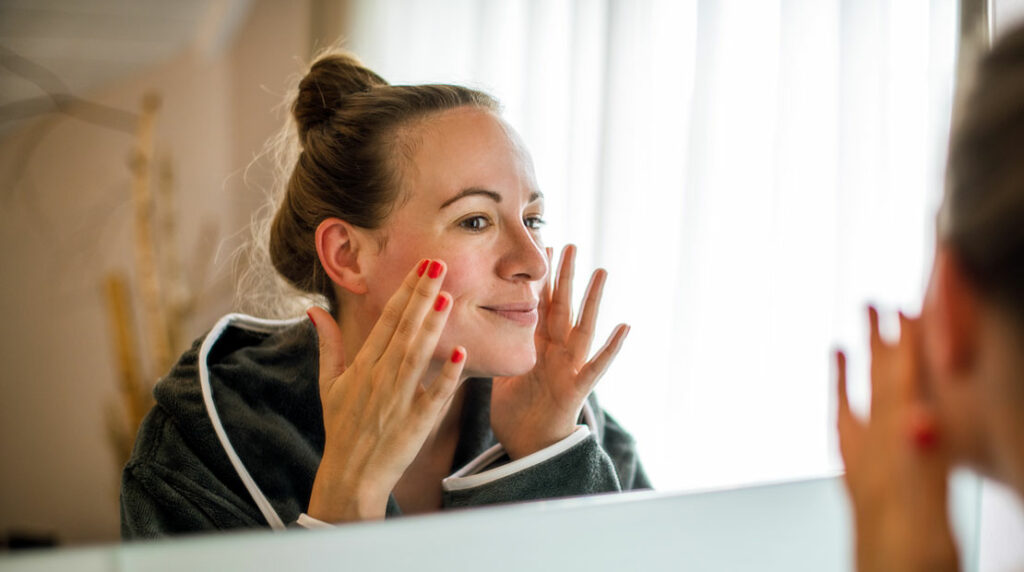 Frau im Bademantel sieht sich im Spiegel an und lächelt