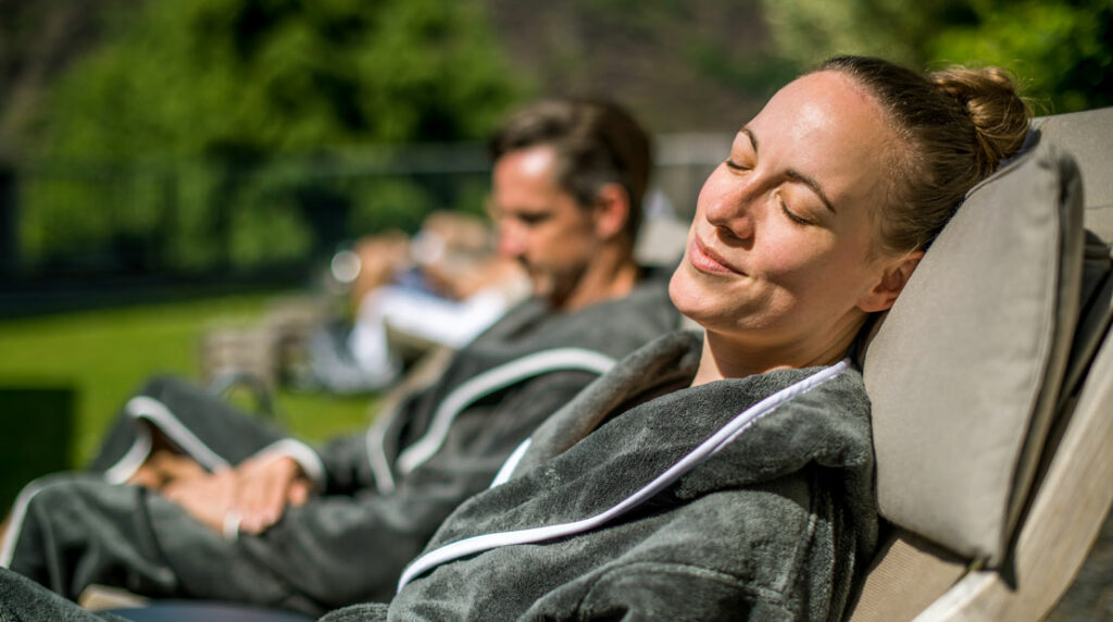 Frau und Mann im Bademantel auf Liegen im Außenbereich